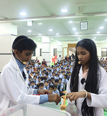 Students Jainam and Jivika conducting a science demonstration during a school assembly