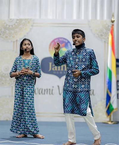 Jainam and Jivika speaking on stage at a youth event